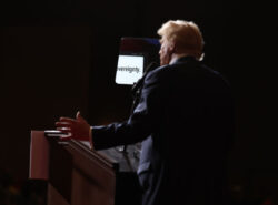 Trumpt kuvattu takaa. Pimeät valot, vain miehen etupuoli valaistu. Hänen edessään näkyy pieni lasi/peili, missä digitaalisesti sana "sovereignty".