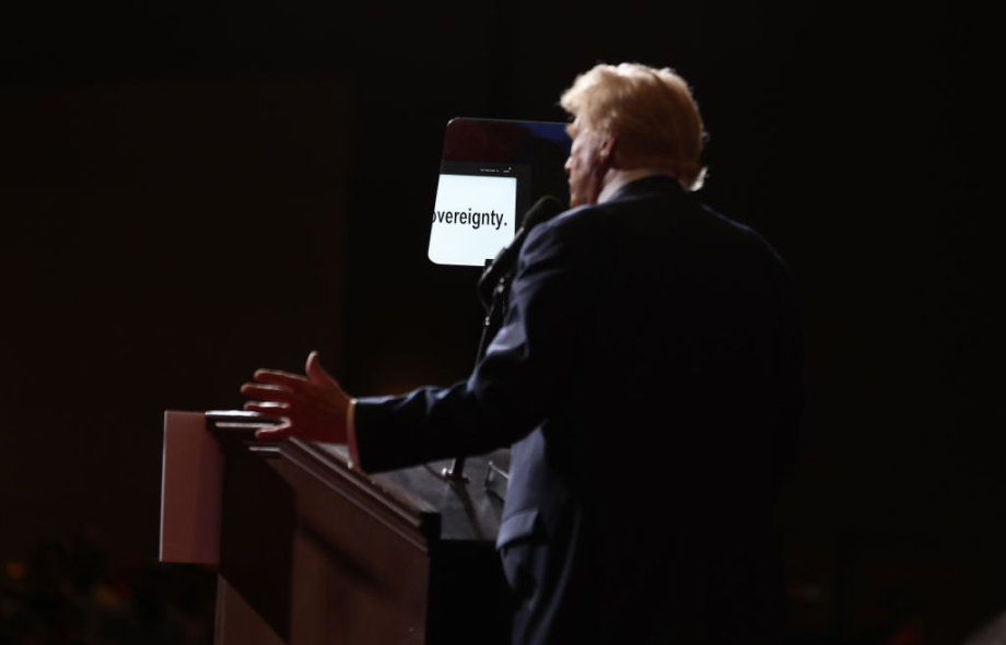 Trumpt kuvattu takaa. Pimeät valot, vain miehen etupuoli valaistu. Hänen edessään näkyy pieni lasi/peili, missä digitaalisesti sana "sovereignty".