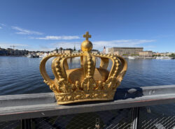 Etualalla sillan kaiteeseen kiinnitetty Kruunu. Taustalla Ruotsin kuninkaanlinna. Kuva toukokuussa 2026.