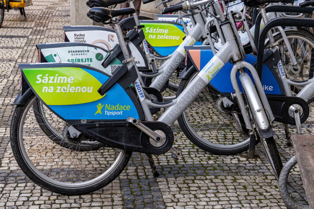 Nextbike-kaupunkipyöriä pysäköitynä Prahan mukulakivikadulla. Pyörien lokasuojissa on vedonlyöntiyhtiö Tipsportin säätiön mainokset tekstillä Sázíme na zelenou.