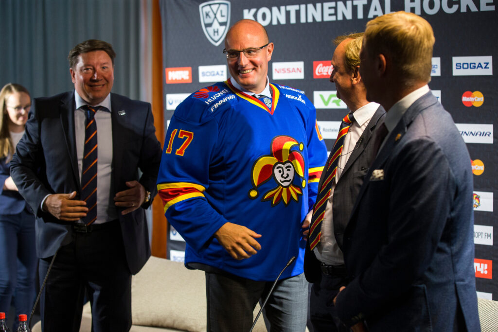 Dmitri Tshernishenko vierellään Jari Kurri ja Hjallis Harkimo sekä Jukka Kohonen. Tshernishenkolla päällään Jokerit paita missä esimerkiksi Veikkaus, Huawei ja Finnair logot. Taustalla KHL seinä missä esimerkiksi Nissan, Coca Cola, Mastercard.