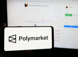Polymarketin logo puhelimella, taustalla tietokoneen näytöllä auki Polymarket.