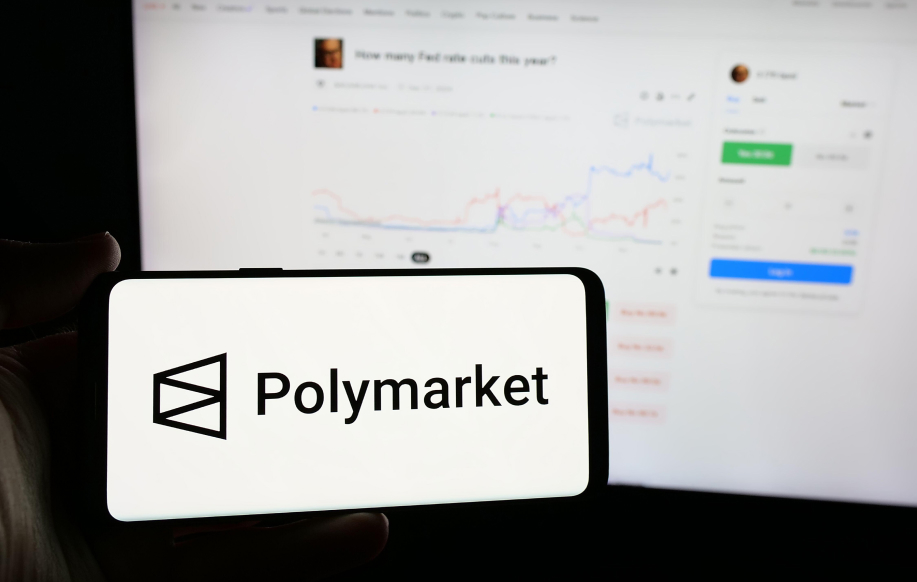 Polymarketin logo puhelimella, taustalla tietokoneen näytöllä auki Polymarket.