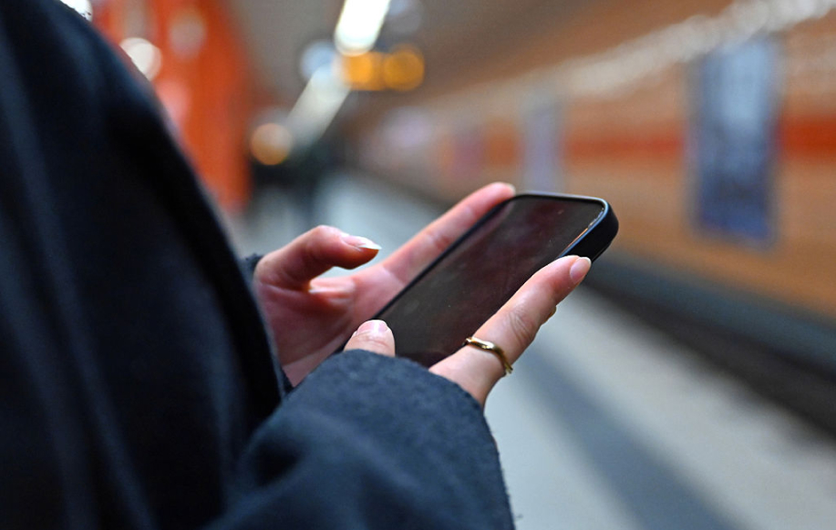 Nainen käyttää puhelinta metrossa Berliinissä. Lähikuva puhelimesta mutta ruutu mustana.