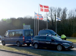 Tanskassa poliisiautot ja poliisit estävät rajan. Taustalla Pohjoismaiden lippuja rajan yhteydessä. Kuvattu Tanskan puolelta.