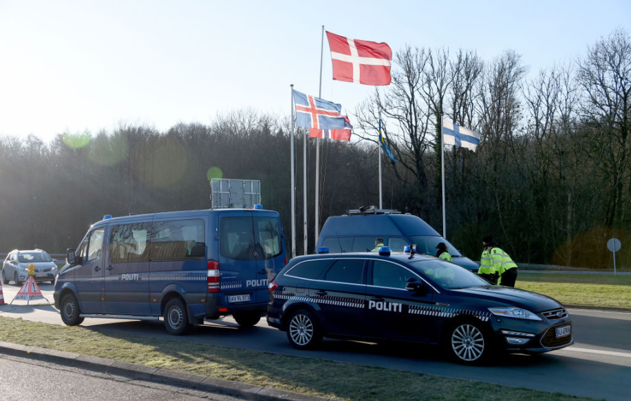 Tanskassa poliisiautot ja poliisit estävät rajan. Taustalla Pohjoismaiden lippuja rajan yhteydessä. Kuvattu Tanskan puolelta.