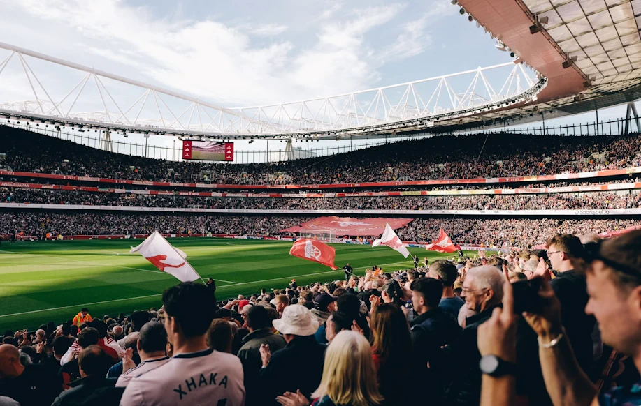 Täysi Emirates Stadium Valioliigaottelun alla. Arsenal-kannattajat täyttävät katsomot ja kentän laidalla liehuu seuran lippuja.