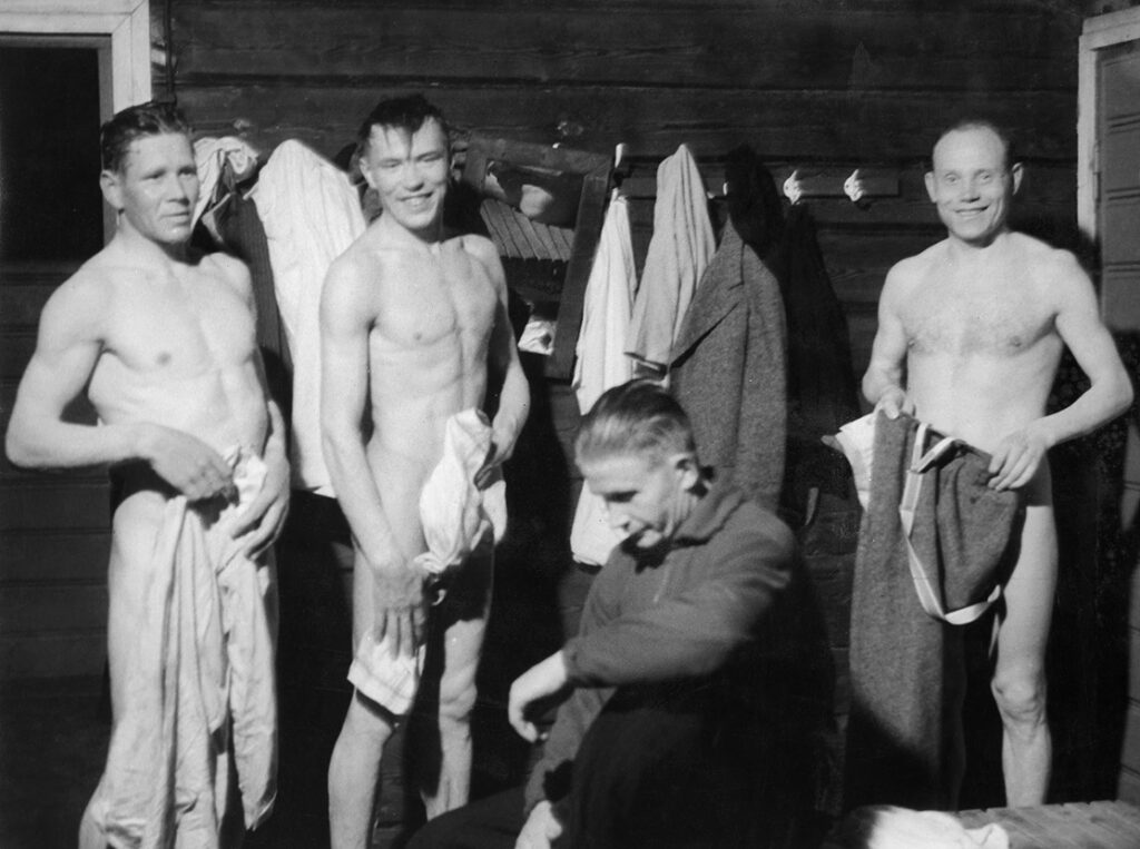 Miehet saunan edustalla. Kolme miehistä alasti. Vasemmalla Paavo Nurmi hymyilee kameralle. Kundit tiukassa kunnossa!