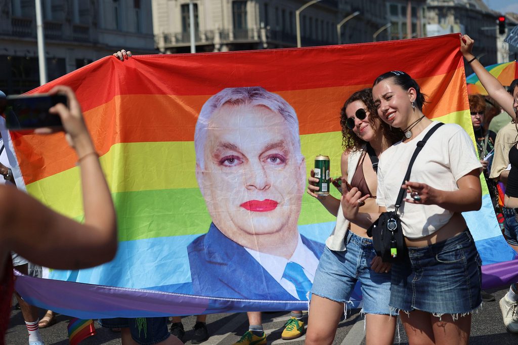 Kaksi nuorta naista ottaa kuvaansa sateenkaarilipun kanssa missä Orbanin kuva. Orban meikattu.